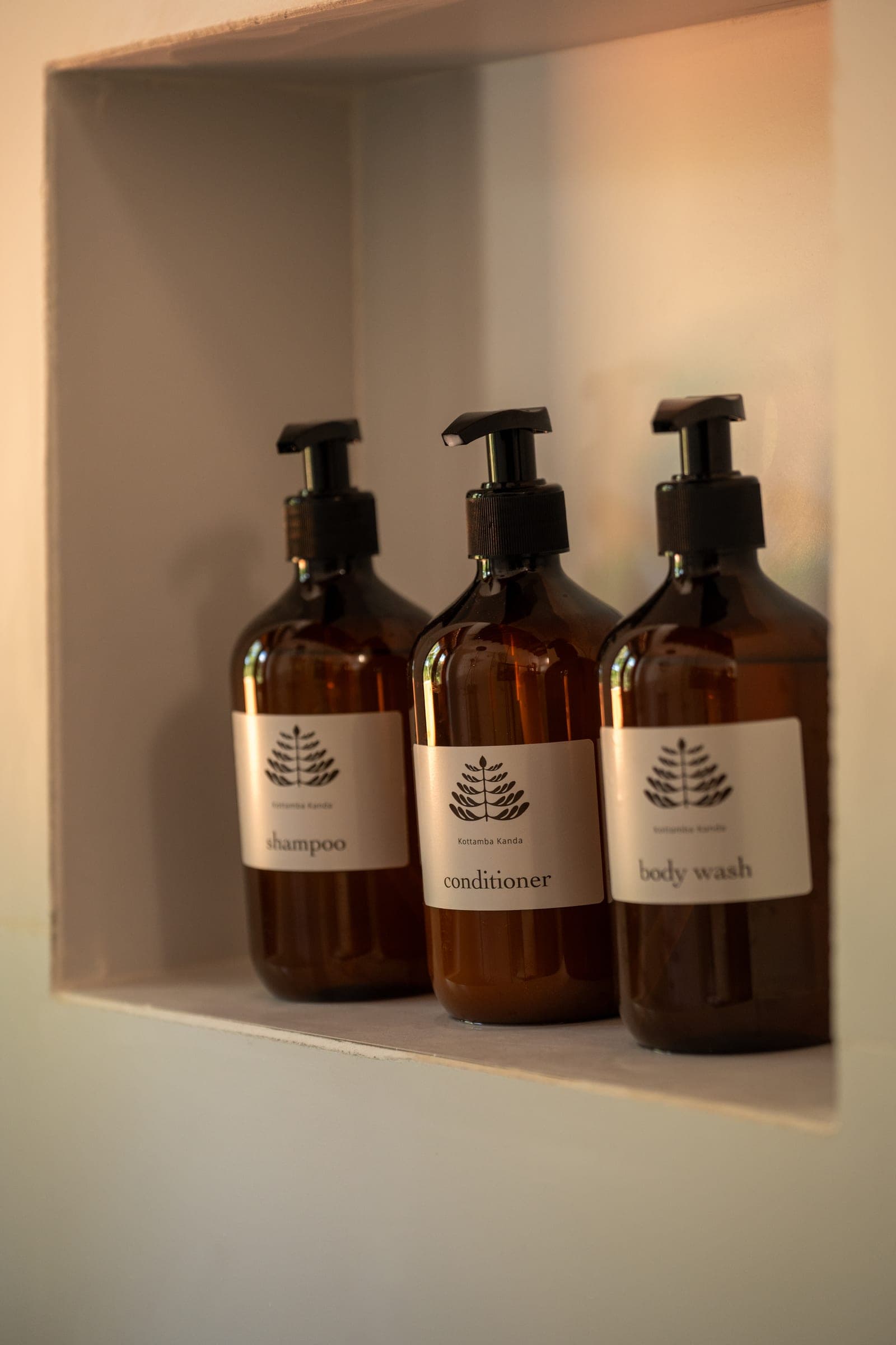 Kottamba Kanda's own shampoo, conditioner and body wash in amber bottles in a bathroom niche