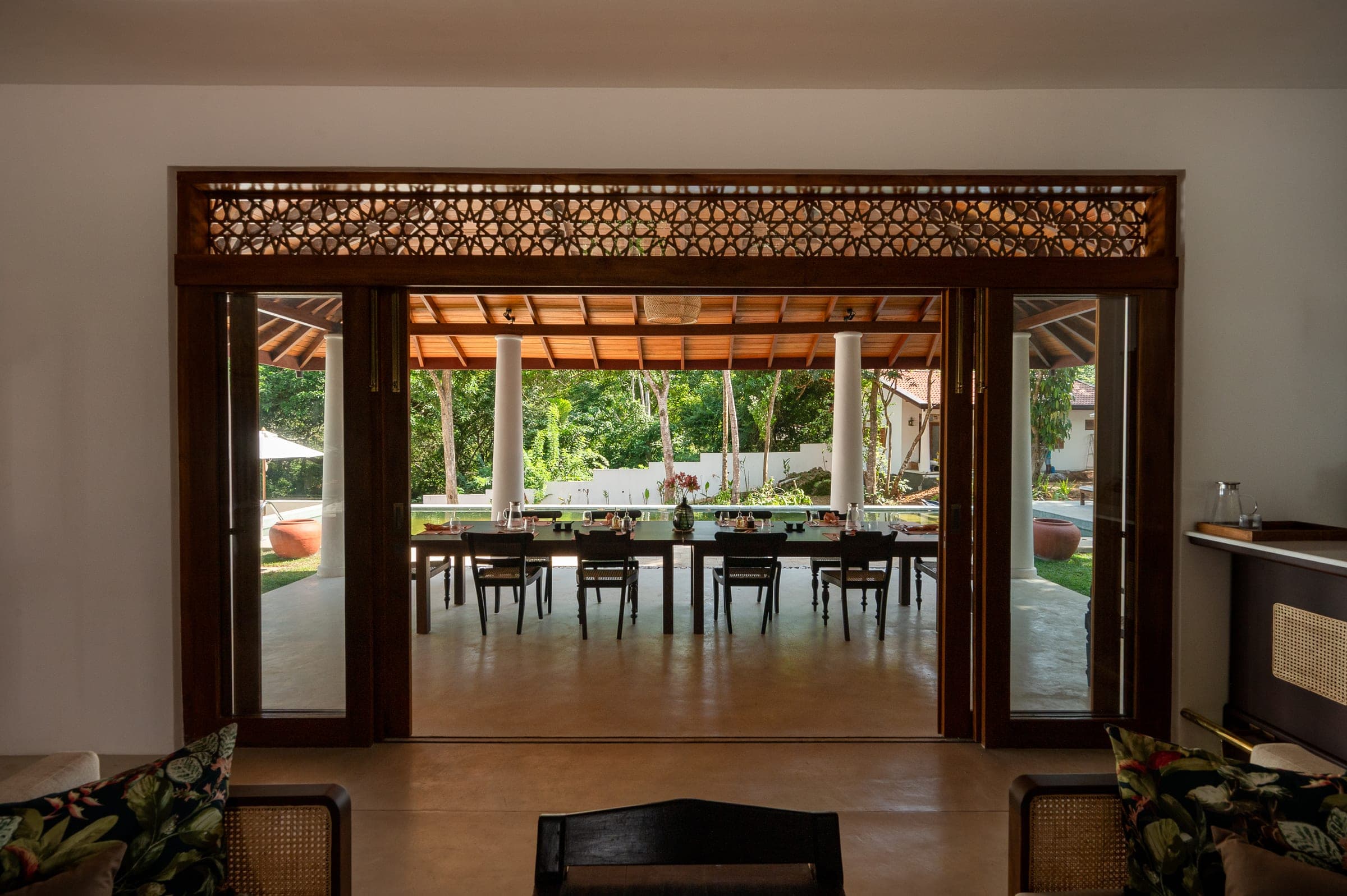 The dining verandah at Kottamba Kanda seen from the living room, the long table set between white columns with the pool beyond