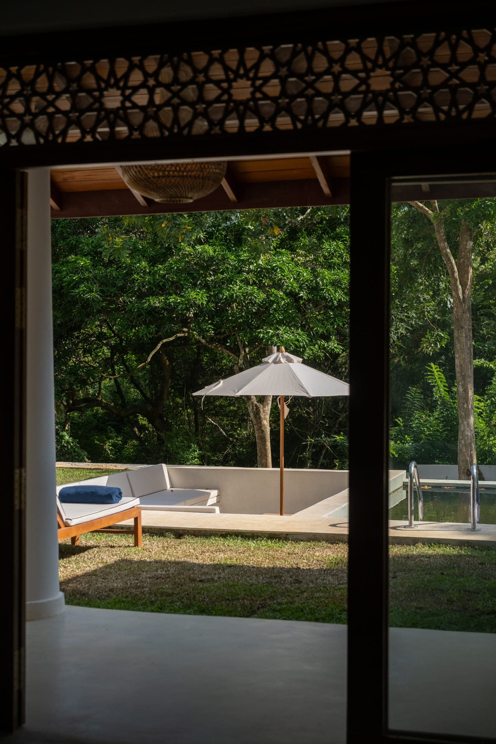 The sunken pool lounge and parasol at Kottamba Kanda, seen through the open doors of a ground-floor bedroom