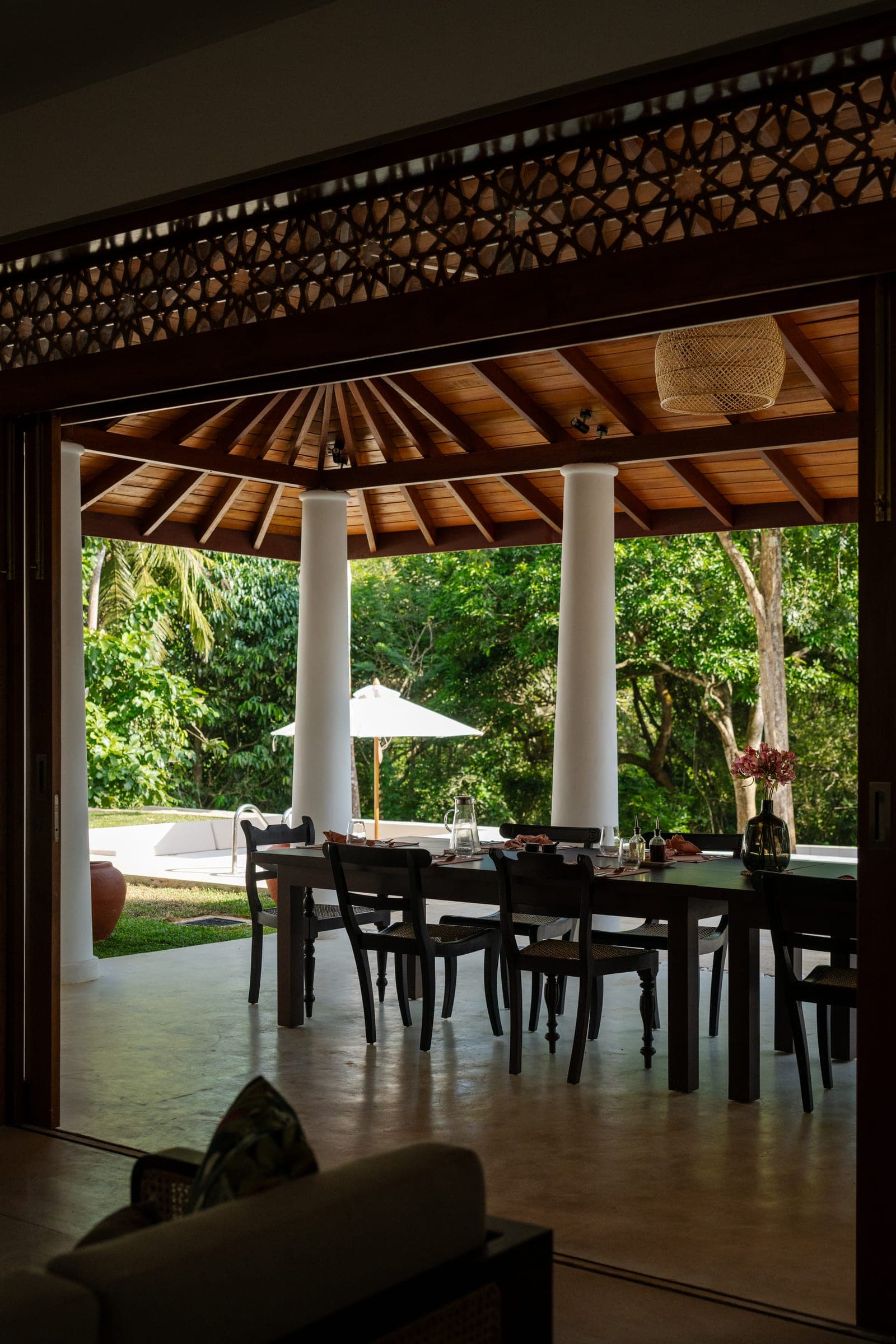 The dining table on the verandah at Kottamba Kanda, under the timber roof with the pool and garden beyond